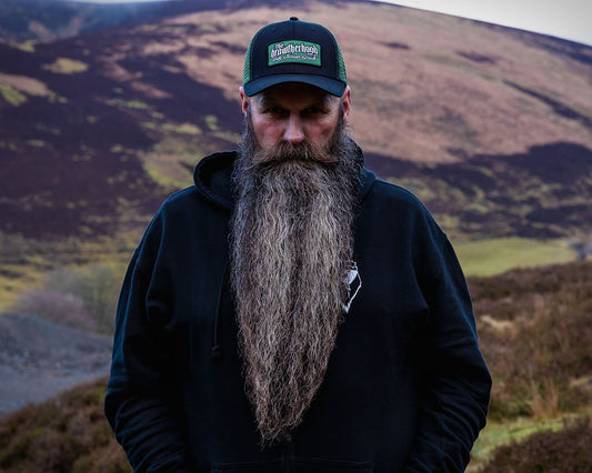 rugged man brushing mid-growth beard in natural Scottish setting