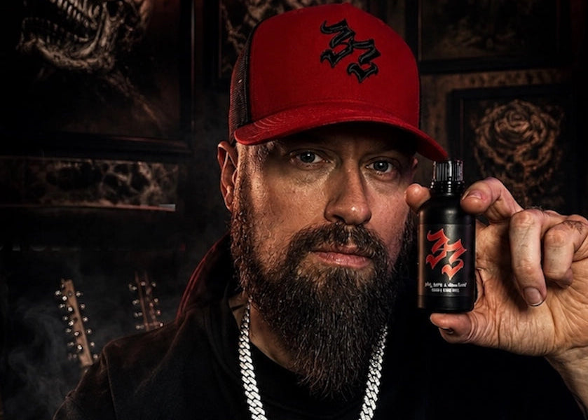 Man holding a bottle of beard oil with a dark, themed background, Andy James Five Finger Death Punch